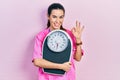 Young brunette nutritionist woman holding scale doing ok sign with fingers, smiling friendly gesturing excellent symbol