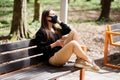 Young brunette in a protective mask in the park sitting on a bench. Woman with closed eyes enjoying the air and sunny weather