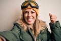 Young brunette skier woman wearing snow clothes and ski goggles make selfie by camera screaming proud and celebrating victory and Royalty Free Stock Photo