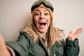 Young brunette skier woman wearing snow clothes and ski goggles make selfie by camera very happy and excited, winner expression