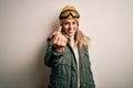 Young brunette skier woman wearing snow clothes and ski goggles over white background Beckoning come here gesture with hand