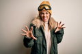 Young brunette skier woman wearing snow clothes and ski goggles over white background smiling funny doing claw gesture as cat,