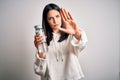 Young brunette sporty woman with blue eyes holding water bottle over white background with open hand doing stop sign with serious Royalty Free Stock Photo