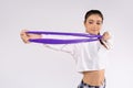 Young brunette stretches an elastic band in front of the camera looking to the side. White studio background.