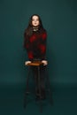 Young brunette teen girl stands near the chair over dark-green background, isolated in studio Royalty Free Stock Photo