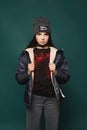 Young brunette teen model girl, in jacket and hat, stands over dark-green background, Royalty Free Stock Photo