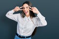 Young brunette teenager doing peace gesture close to eyes smiling and laughing hard out loud because funny crazy joke Royalty Free Stock Photo