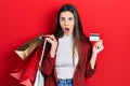 Young brunette teenager holding shopping bags and credit card afraid and shocked with surprise and amazed expression, fear and Royalty Free Stock Photo