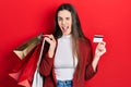 Young brunette teenager holding shopping bags and credit card winking looking at the camera with sexy expression, cheerful and Royalty Free Stock Photo