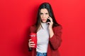 Young brunette teenager talking on smartphone and drinking coffee relaxed with serious expression on face Royalty Free Stock Photo