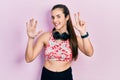 Young brunette teenager wearing gym clothes and using headphones showing and pointing up with fingers number eight while smiling Royalty Free Stock Photo