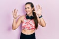 Young brunette teenager wearing gym clothes and using headphones showing and pointing up with fingers number ten while smiling Royalty Free Stock Photo