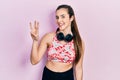 Young brunette teenager wearing gym clothes and using headphones showing and pointing up with fingers number three while smiling Royalty Free Stock Photo