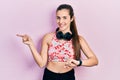 Young brunette teenager wearing gym clothes, using headphones and smart watch smiling happy pointing with hand and finger to the Royalty Free Stock Photo