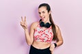 Young brunette teenager wearing gym clothes and using headphones smiling with happy face winking at the camera doing victory sign Royalty Free Stock Photo