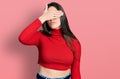 Young brunette teenager wearing red turtleneck sweater covering eyes with hand, looking serious and sad Royalty Free Stock Photo