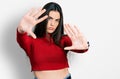 Young brunette teenager wearing red turtleneck sweater doing frame using hands palms and fingers, camera perspective Royalty Free Stock Photo