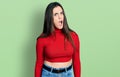 Young brunette teenager wearing red turtleneck sweater in shock face, looking skeptical and sarcastic, surprised with open mouth Royalty Free Stock Photo