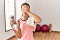 Young brunette teenager wearing sportswear holding water bottle covering eyes with hand, looking serious and sad Royalty Free Stock Photo