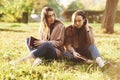 Young brunette twin sisters sitting close to each other with eyes closed on the grass,legs slightly bent in knees and Royalty Free Stock Photo