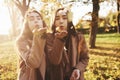 Young brunette twin sisters standing close to each other and blowing confetti into camera, wearing casual coat in autumn Royalty Free Stock Photo