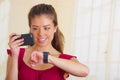 Young brunette wearing red top facing camera, holding mobile phone and looking at smart watch, white studio background Royalty Free Stock Photo