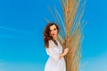 young brunette in white dress sianding with palm leaves on a tropical beach. Summer vacation concept. Royalty Free Stock Photo