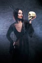 A young brunette witch holding a human skull