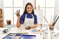 Young brunette woman at art studio with painted hands showing and pointing up with fingers number four while smiling confident and Royalty Free Stock Photo