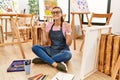 Young brunette woman at art studio sitting on the floor excited for success with arms raised and eyes closed celebrating victory Royalty Free Stock Photo