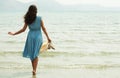 Young woman in a blue dress walking barefoot on a beach and dangles his feet in the water.