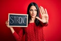 Young brunette woman with blue eyes holding blackboard with strong word message with open hand doing stop sign with serious and Royalty Free Stock Photo