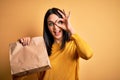 Young brunette woman with blue eyes holding delivery paper bag with food with happy face smiling doing ok sign with hand on eye Royalty Free Stock Photo