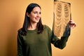 Young brunette woman with blue eyes holding xray of lungs over yellow background with a happy face standing and smiling with a