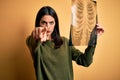 Young brunette woman with blue eyes holding xray of lungs over yellow background pointing with finger to the camera and to you, Royalty Free Stock Photo