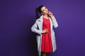 Young brunette woman with blue eyes, in red dress and coat, posing at violet background Royalty Free Stock Photo