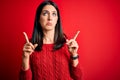 Young brunette woman with blue eyes wearing casual sweater over isolated red background Pointing up looking sad and upset,