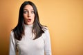 Young brunette woman with blue eyes wearing casual sweater over isolated yellow background afraid and shocked with surprise