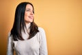 Young brunette woman with blue eyes wearing casual sweater over isolated yellow background looking away to side with smile on Royalty Free Stock Photo