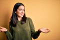 Young brunette woman with blue eyes wearing green casual sweater over yellow background smiling showing both hands open palms, Royalty Free Stock Photo