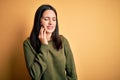 Young brunette woman with blue eyes wearing green casual sweater over yellow background touching mouth with hand with painful Royalty Free Stock Photo