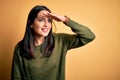 Young brunette woman with blue eyes wearing green casual sweater over yellow background very happy and smiling looking far away Royalty Free Stock Photo