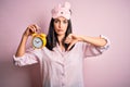 Young brunette woman with blue eyes wearing pajama and eye mask holding alarm clock with angry face, negative sign showing dislike Royalty Free Stock Photo