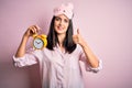 Young brunette woman with blue eyes wearing pajama and eye mask holding alarm clock happy with big smile doing ok sign, thumb up Royalty Free Stock Photo