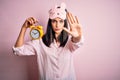 Young brunette woman with blue eyes wearing pajama and eye mask holding alarm clock with open hand doing stop sign with serious Royalty Free Stock Photo