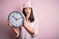 Young brunette woman with blue eyes wearing pajama holding big clock at night time scared in shock with a surprise face, afraid Royalty Free Stock Photo