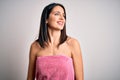 Young brunette woman with blue eyes wearing shower towel after bath over white background looking away to side with smile on face, Royalty Free Stock Photo