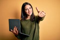 Young brunette woman with blue eyes working using computer laptop over yellow background approving doing positive gesture with Royalty Free Stock Photo