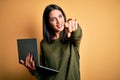 Young brunette woman with blue eyes working using computer laptop over yellow background pointing to you and the camera with Royalty Free Stock Photo