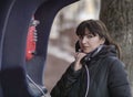 Young brunette woman calling from a red street payphone, looking directly at the camera Royalty Free Stock Photo